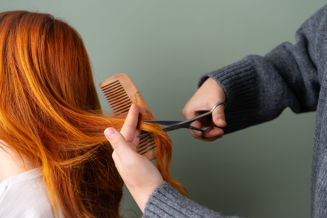 creative Close-up of red hair being trimmed with scissors and comb on green background.